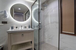 A modern bathroom with a glass-enclosed shower, a round mirror, and a vanity with a marble countertop.