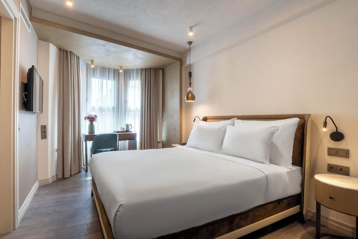 A hotel room with a large bed, bedside table, and a desk with a chair.
