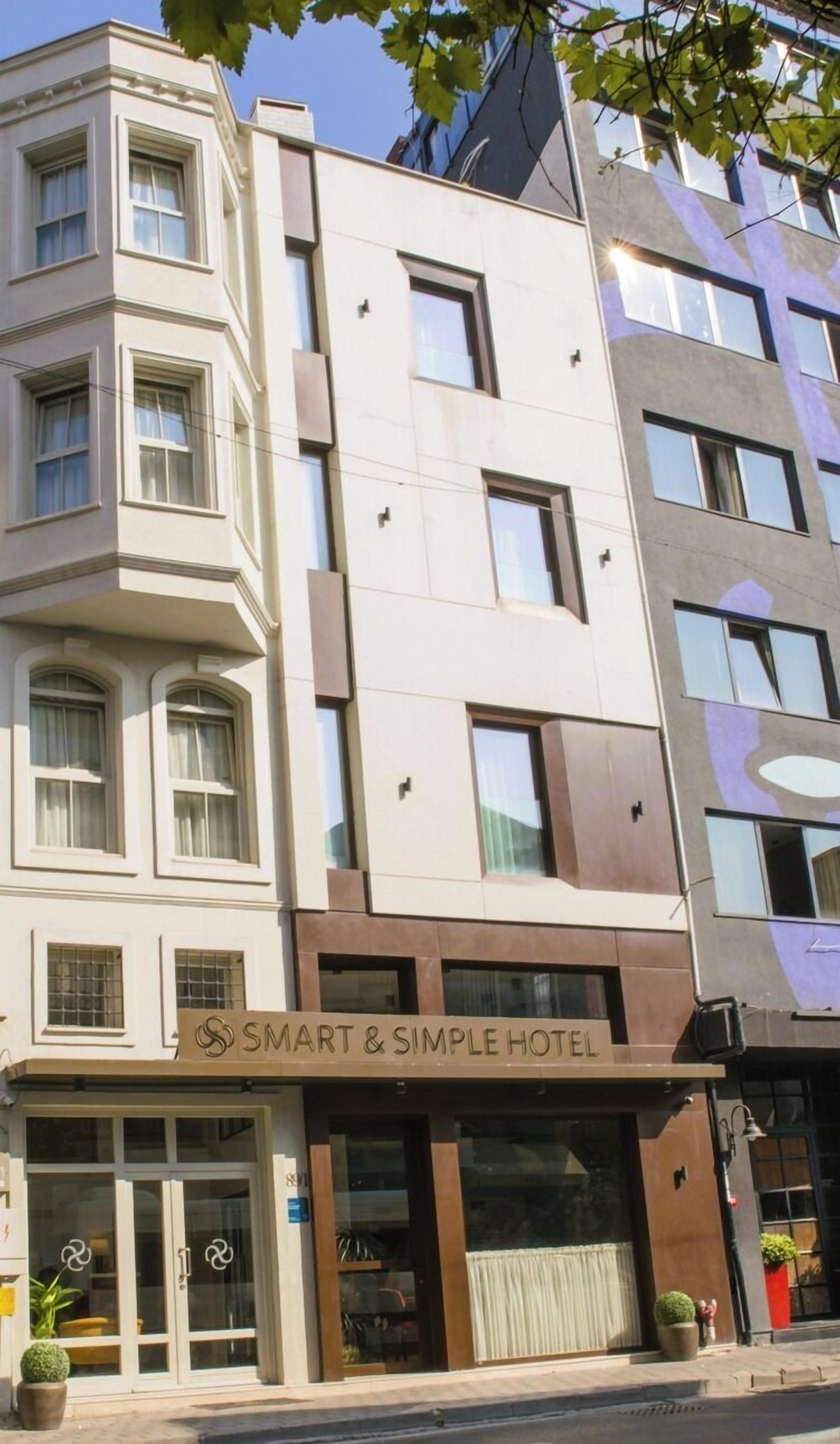Un hotel de varios pisos con fachada moderna, que presenta un cartel llamativo de 'SMART & SIMPLE HOTEL' a nivel de calle.