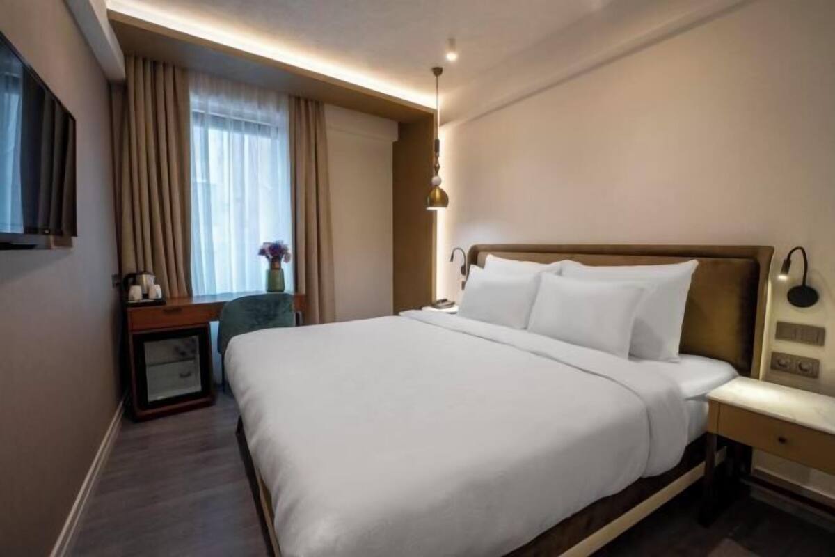 A hotel room with a large bed, bedside tables, a TV, and a window with curtains.