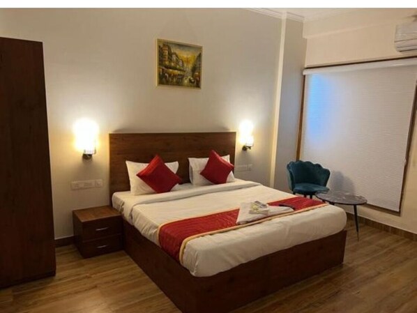 A hotel room with a wooden bed, two bedside lamps, a small table, and a chair. - Hotel Sunlight Brown By GRB (Greater Noida)