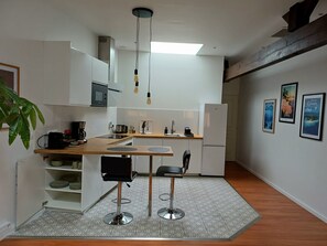 A compact kitchen with a wooden countertop, two bar stools, a refrigerator, and a coffee maker. - Nice, comfortable one-bedroom apartment near Saint-Jean Station (Bordeaux)