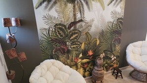 Ein Zimmer mit einem weißen, gepolsterten Sessel, einem kleinen Tisch und einem dekorativen Wandbild.