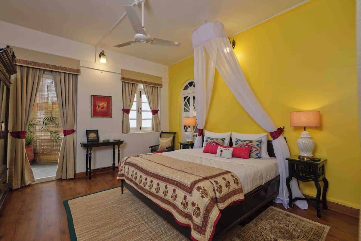 Une chambre à coucher comprenant un lit, un ventilateur de plafond, une table de chevet, une lampe, une fenêtre avec des rideaux, un bureau et une chaise.