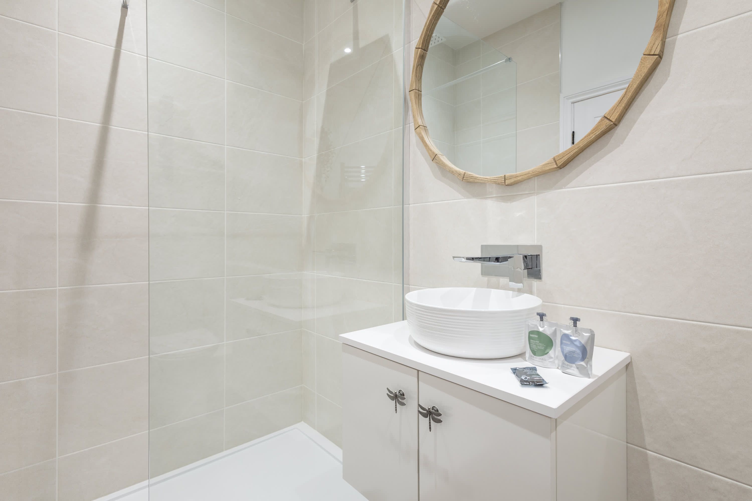A modern bathroom with a large mirror, a round sink, and a shower area.