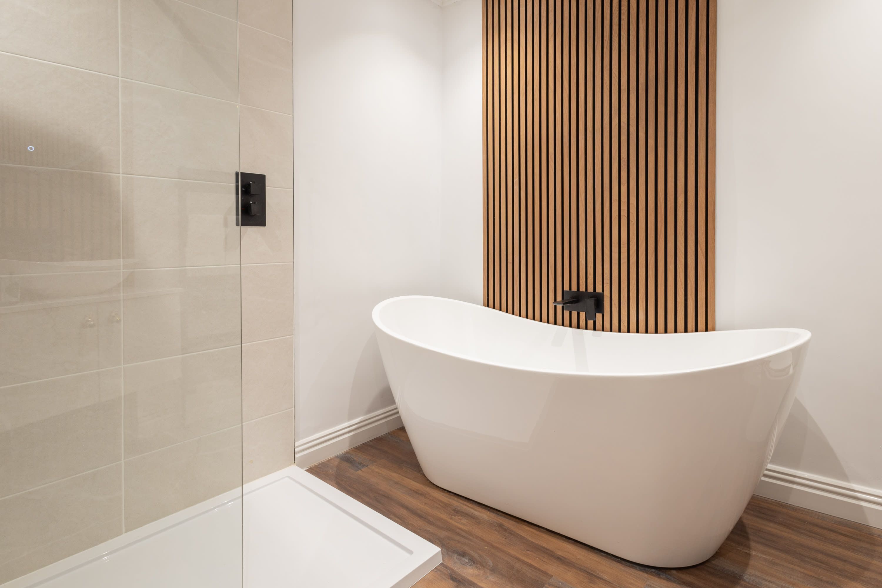 Un bagno moderno con una vasca freestanding, un box doccia in vetro e una parete rivestita in legno.