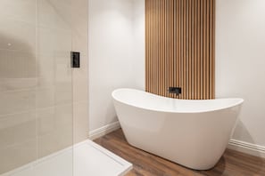 Un baño moderno con una bañera independiente, una cabina de ducha de vidrio y un panel de pared de madera.