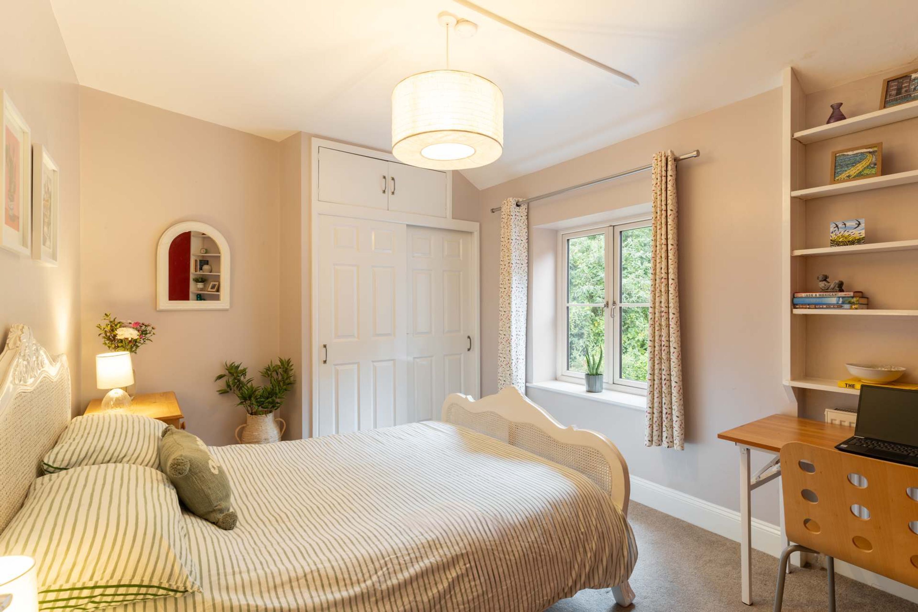 A bedroom with a bed, a desk, a chair, a window with curtains, a bookshelf, and a door.