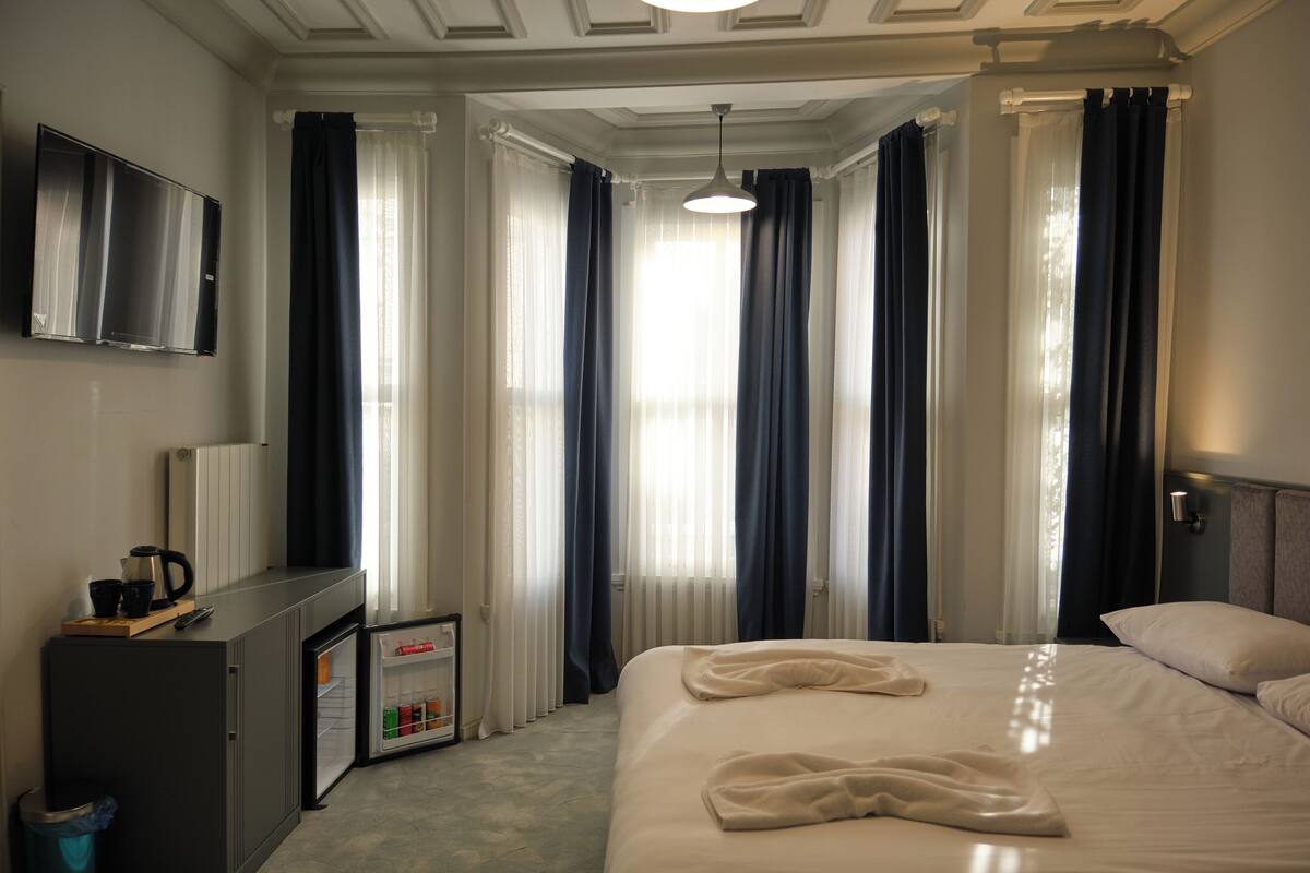A hotel room with a bed, a desk with a computer, a small fridge, and a TV on the wall.
