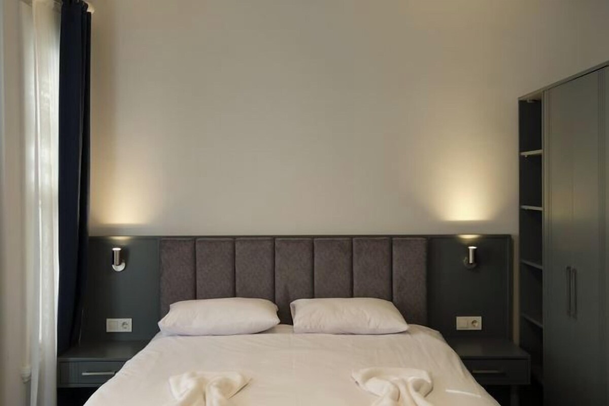 A hotel room with a large bed, two bedside tables, a wardrobe, and a nightstand with a lamp.