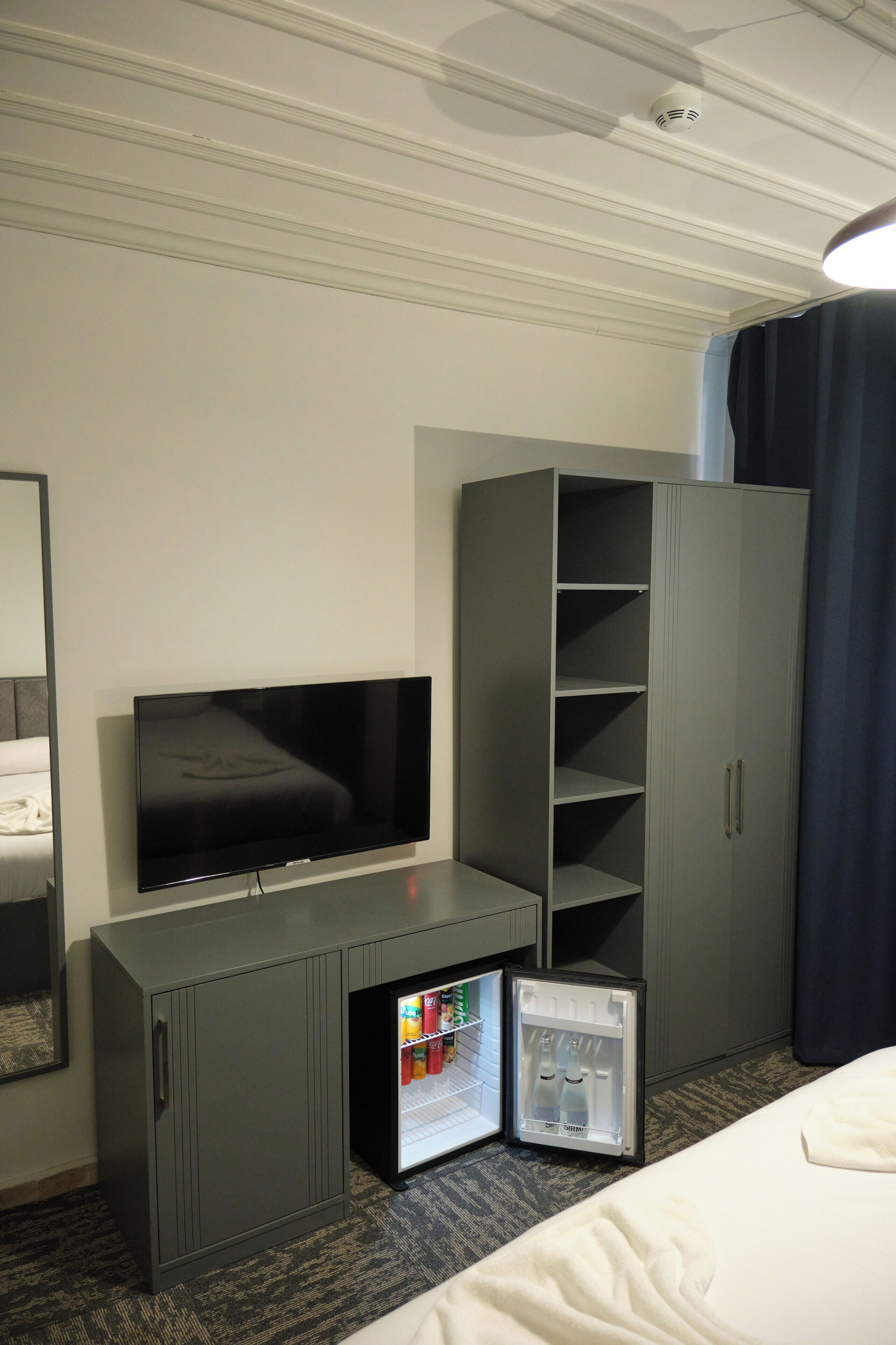 A hotel room with a bed, a television, a wardrobe, and a mini-fridge.