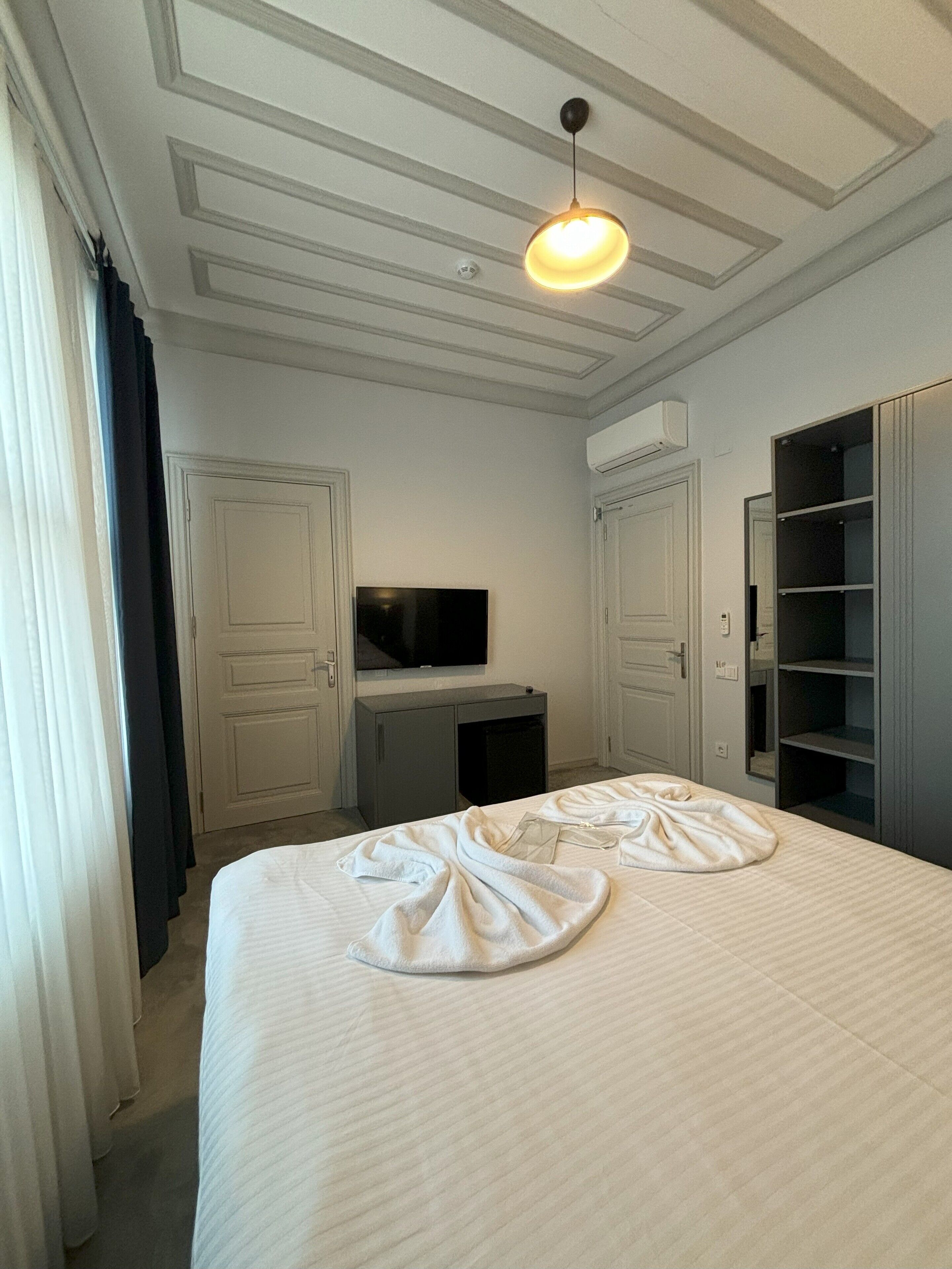 A hotel room with a bed, a television, a wardrobe, and a ceiling light.