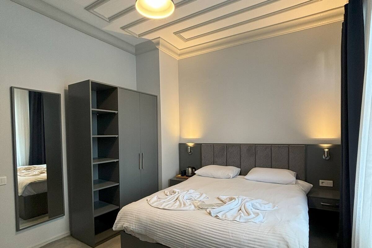 A modern bedroom with a large bed, built-in wardrobe, and a ceiling with a central light fixture.