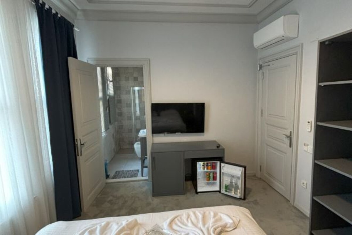 A hotel room with a bed, a TV, a mini-fridge, a wardrobe, and a door leading to a bathroom.