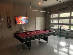 A pool table with balls, a television displaying a fire scene, and a window with a view of the outdoors.