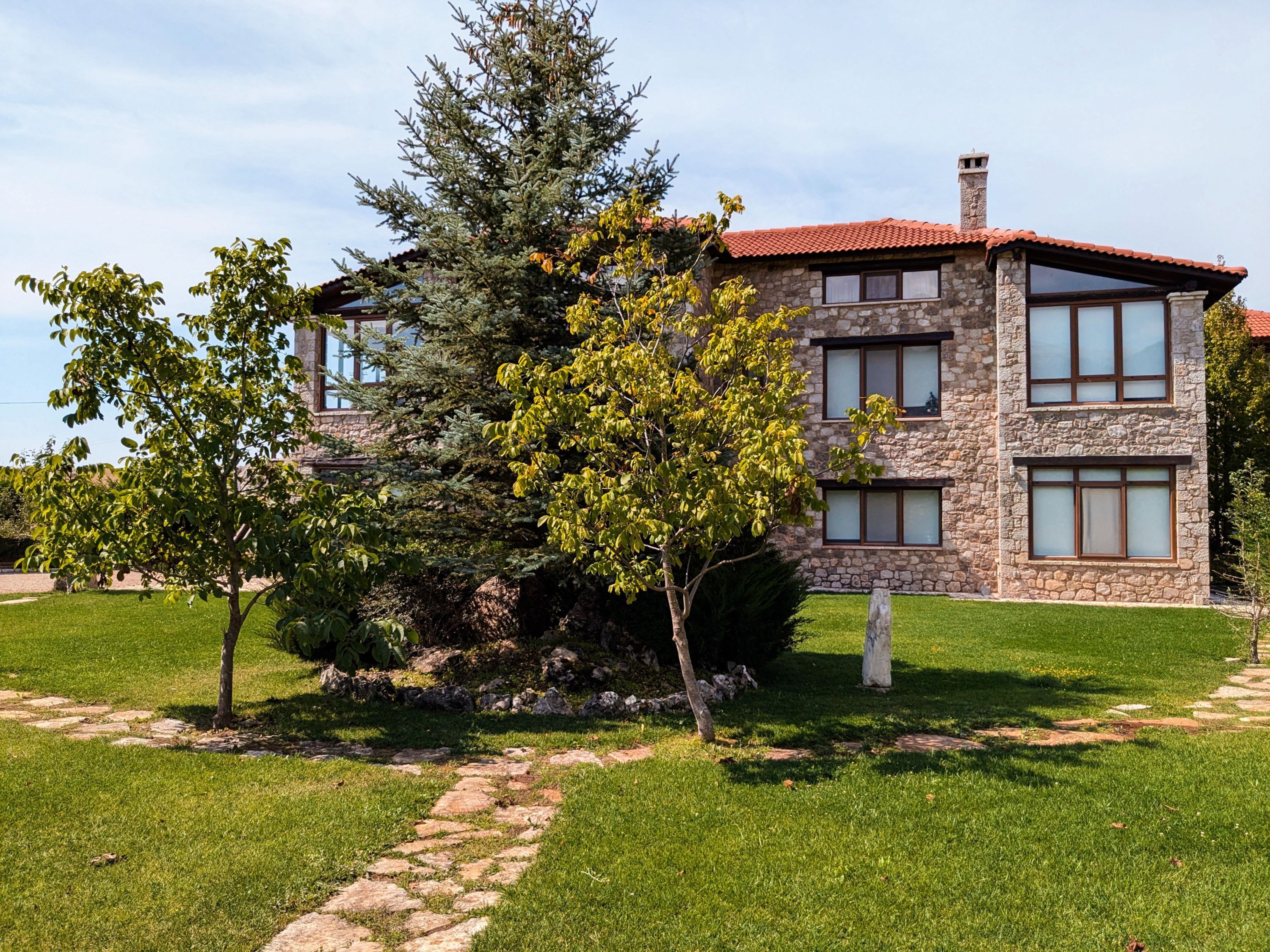 A stone building with a red-tiled roof, multiple windows, and a well-maintained lawn with a stone pathway.