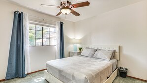 A bedroom with a bed, a ceiling fan, a window with curtains, a nightstand with a lamp, and a trash bin. - Pet-friendly Home w/ Game Room in Las Vegas! (Las Vegas)