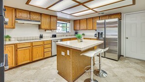 A kitchen with wooden cabinets, a stainless steel refrigerator, and a central island with bar stools. - Pet-friendly Home w/ Game Room in Las Vegas! (Las Vegas)