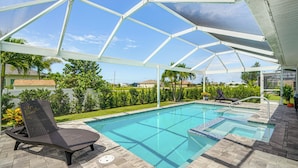 A covered swimming pool with a lounge chair, clear blue water, and a view of the surrounding greenery and houses. - Cape Coral Home w/ Lanai ~ 7 Mi to Marina! (Cape Coral)