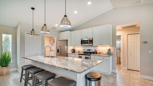 A modern kitchen with white cabinets, stainless steel appliances, and a marble island with bar stools. - Cape Coral Home w/ Lanai ~ 7 Mi to Marina! (Cape Coral)