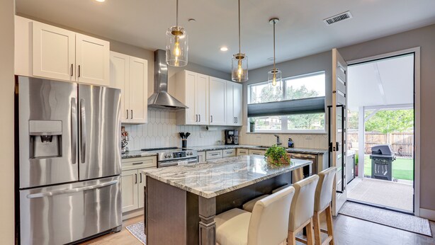A modern kitchen with stainless steel appliances, white cabinets, and a large island with bar stools. - Hot Tub & Mtn-view Rooftop Deck: Golden Home (Golden)