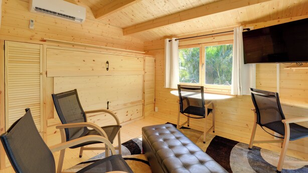 Ein Holzblock-Innenraum mit Deckenventilator, Fernseher und einer Sitzecke mit Sesseln und einer Bank.
