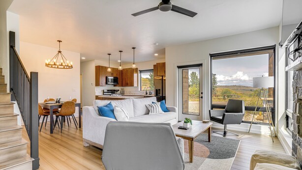 A modern living room with a sofa, coffee table, and chairs, a dining area with a table and chairs, and a kitchen with wooden cabinets and pendant lights. - Mtn-view 'slopeside Chalet' in Granby Ranch! (Granby)