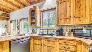 A kitchen with wooden cabinets, a dishwasher, a microwave, and a window with a view of trees. - Ruidoso Retreat w/ Hot Tub & Patio! (Ruidoso)