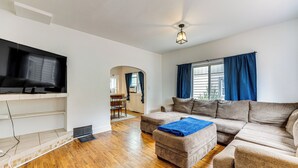 A living room with a sectional sofa, a flat-screen TV, and a wooden floor.