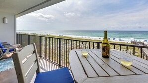 Un balcón con vista a la playa, una mesa con una botella y vasos, y sillones de descanso.