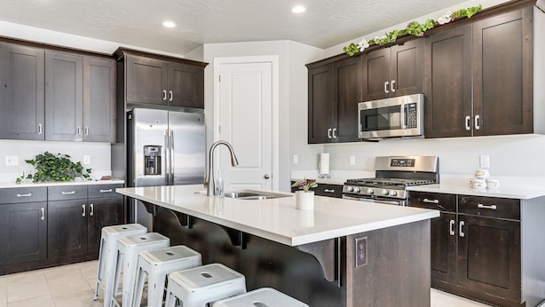 Una cocina moderna con armarios de madera oscura, electrodomésticos de acero inoxidable, una isla grande con taburetes y una encimera blanca.