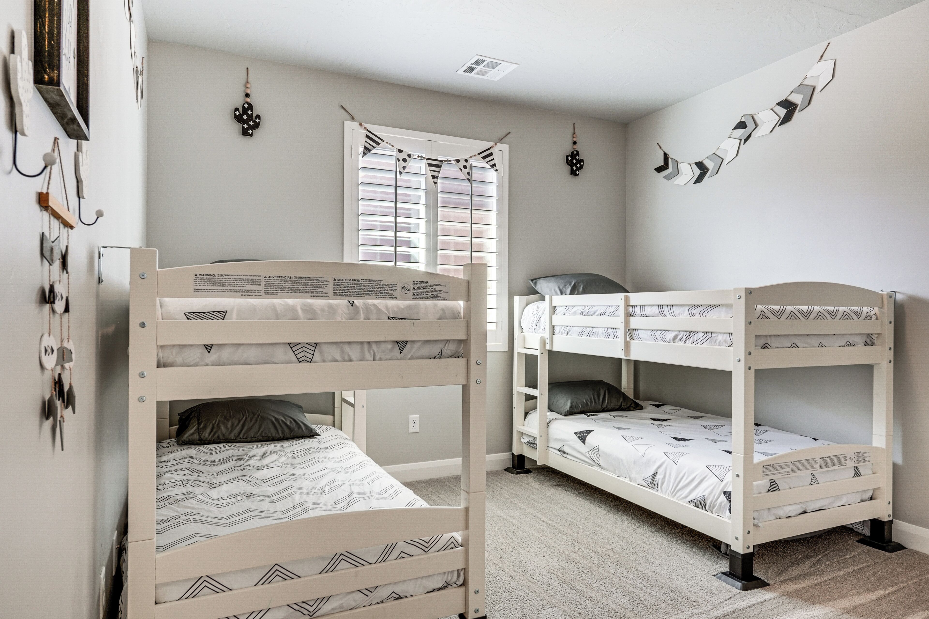 A room with bunk beds, a window with blinds, and wall decorations.