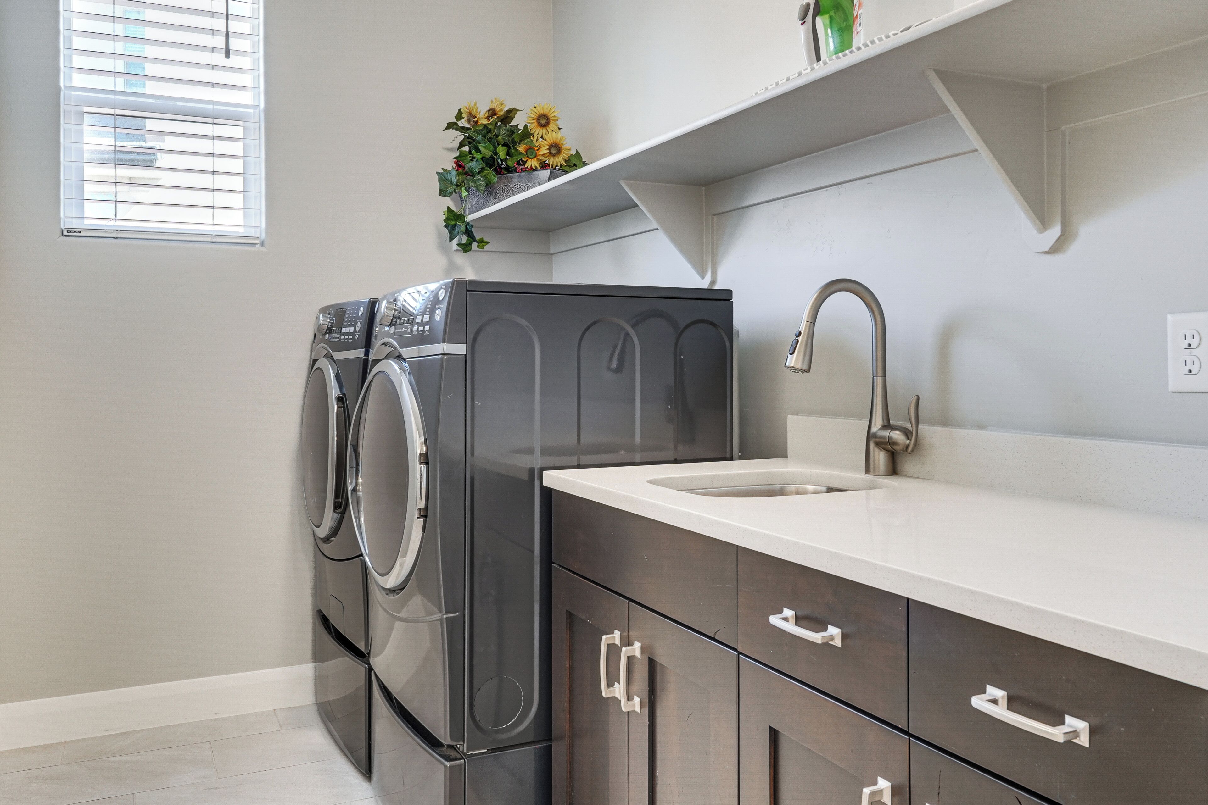 A laundry room with a washing machine, a sink, and a shelf with flowers.