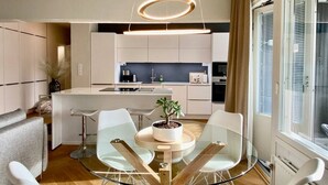 Une cuisine moderne avec des meubles blancs, un îlot central et un coin repas comprenant une table en verre et des chaises blanches.