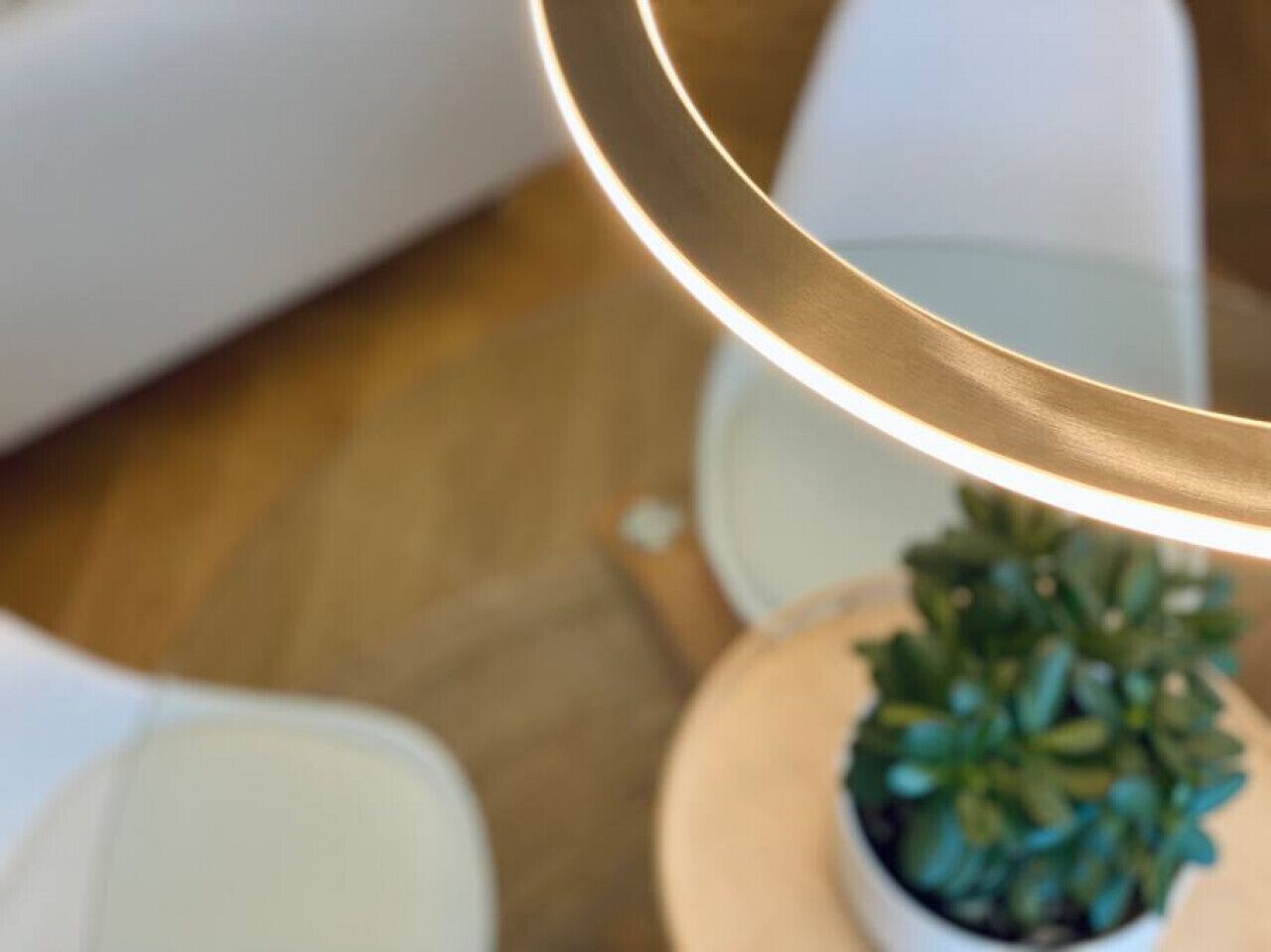 A close-up of a modern lamp with a metallic finish, a small potted plant, and a white chair.