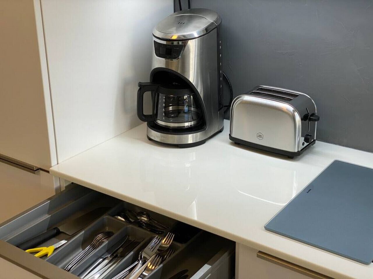 A kitchen with a coffee maker, toaster, and a drawer with utensils.