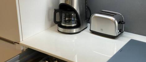 Cozinha com cafeteira, torradeira e gaveta com utensílios.