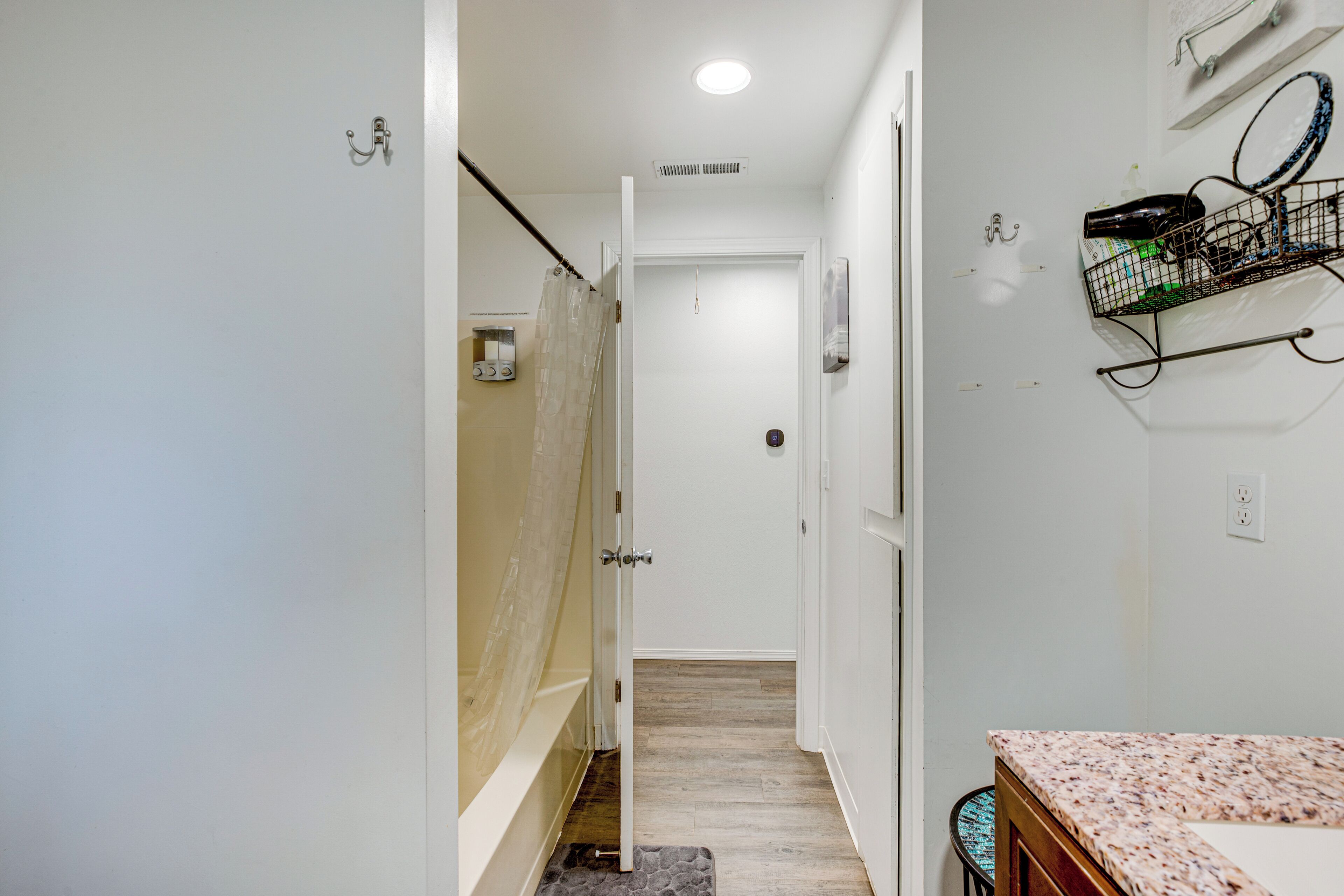 Un pasillo estrecho que conduce a un baño con ducha, lavamanos y toallero.