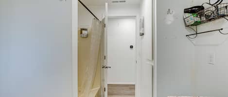 Un pasillo estrecho que conduce a un baño con ducha, lavamanos y toallero.