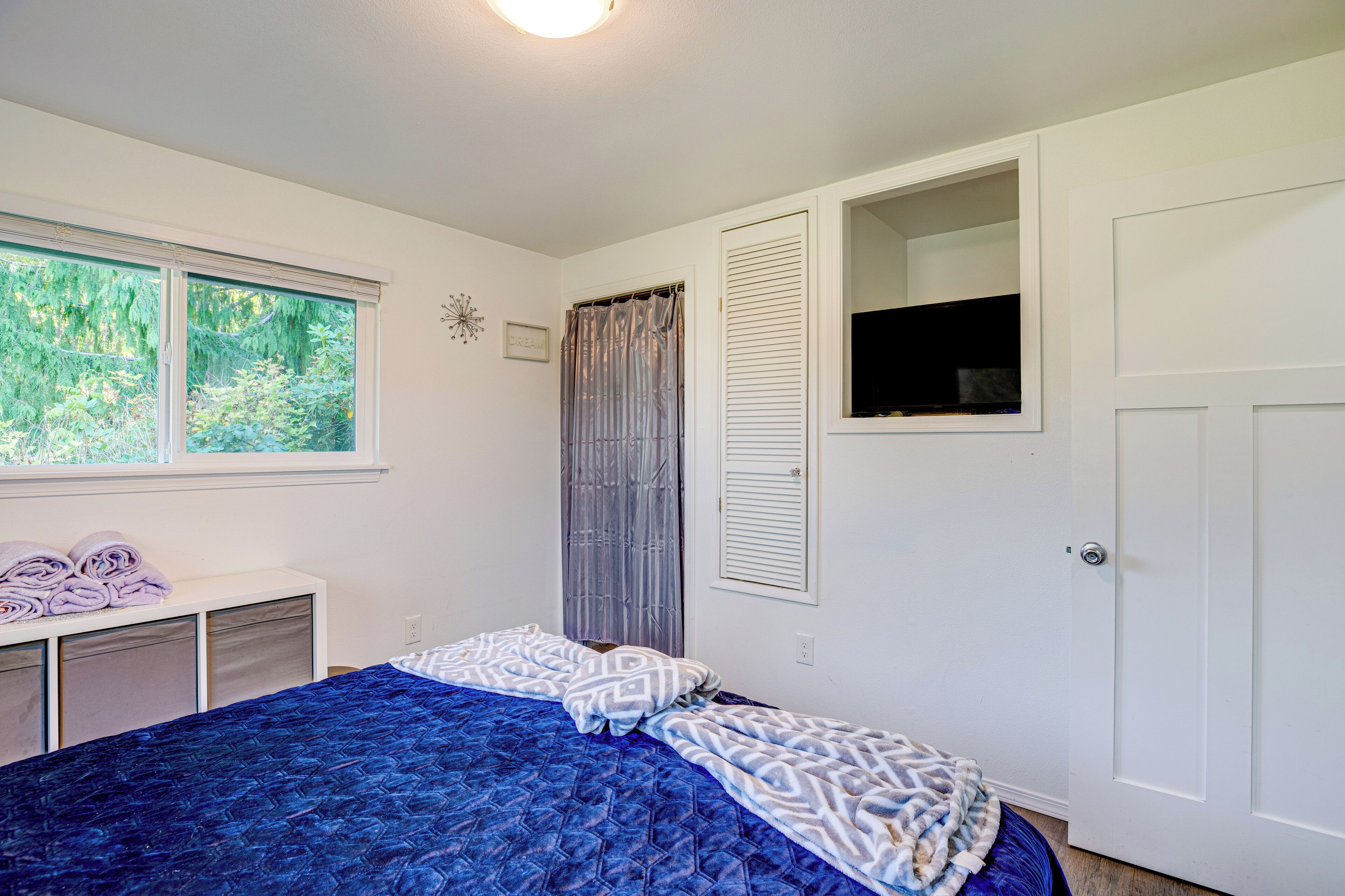 A bedroom with a bed, a window, a door, and a small cabinet.