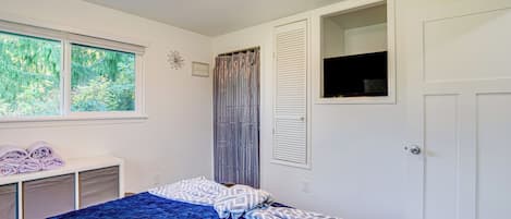 A bedroom with a bed, a window, a door, and a small cabinet.