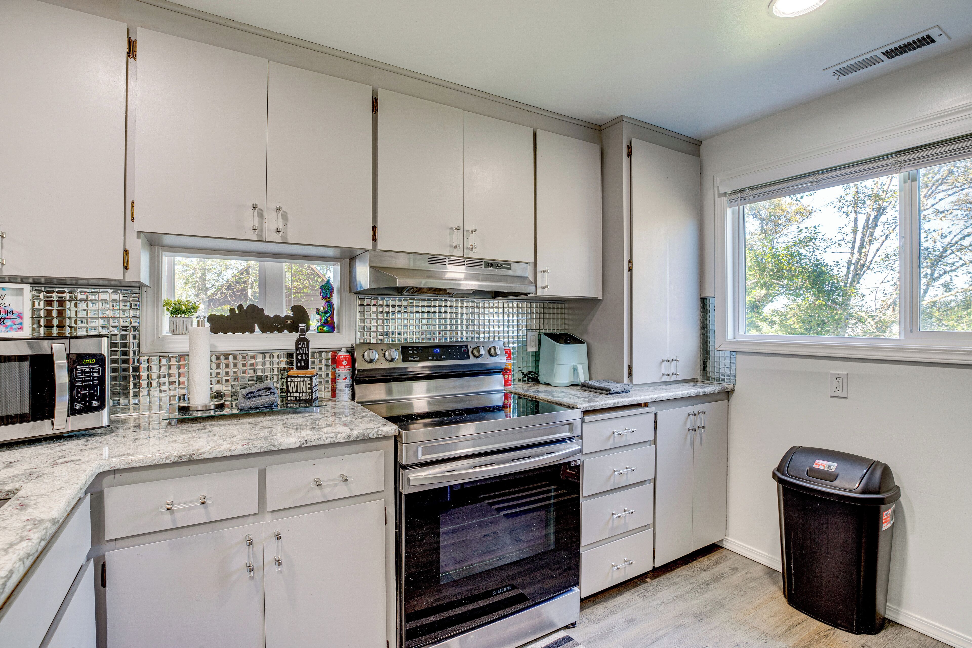 A modern kitchen with white cabinets, stainless steel appliances, and a large window providing natural light.