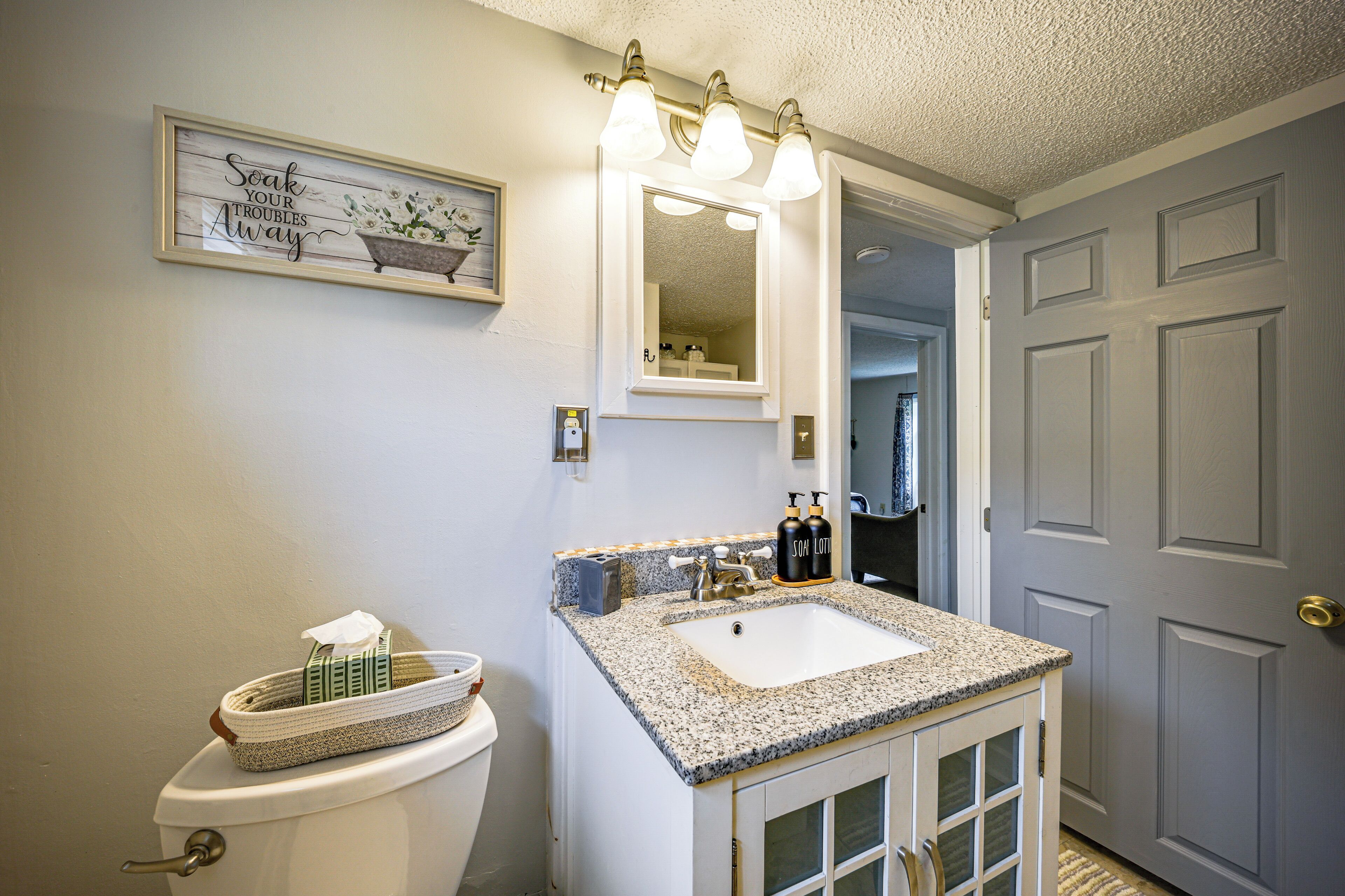 Une salle de bain avec des toilettes blanches, un lavabo doté d’un plan de travail en granit et un miroir au-dessus du lavabo.