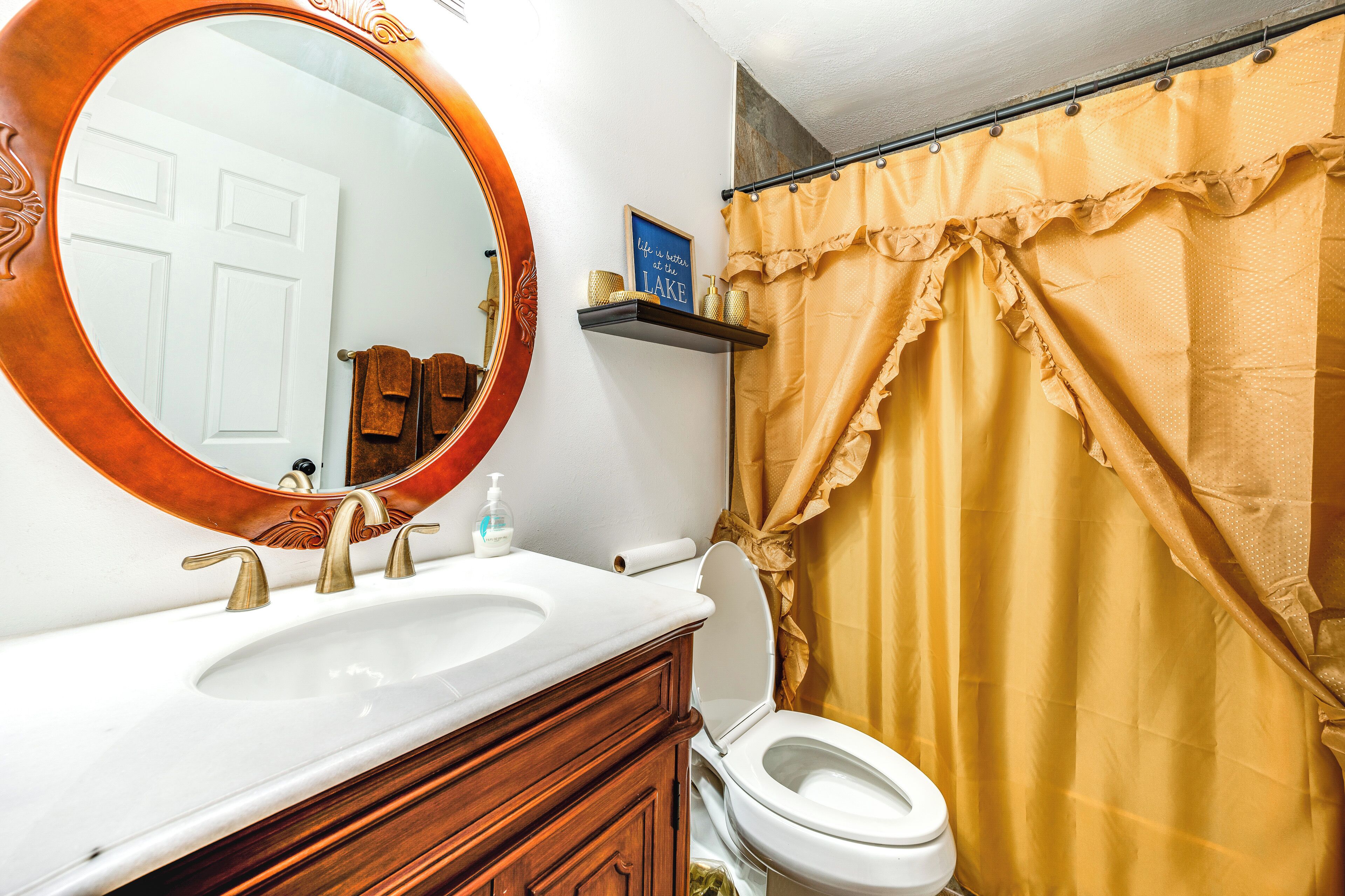 A bathroom with a white sink, a round mirror, a toilet, and a yellow shower curtain.
