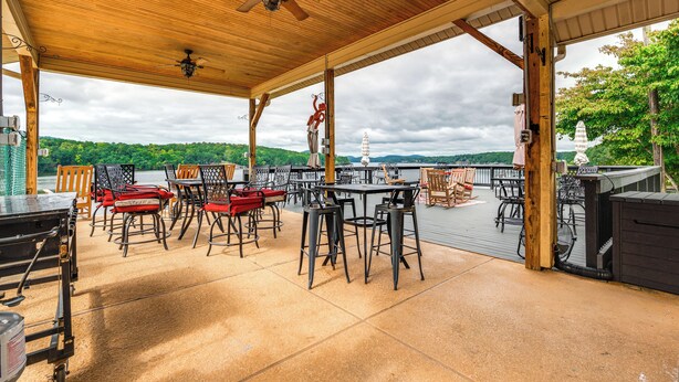 An outdoor patio with tables and chairs, a ceiling fan, and a view of the lake and hills. - Home w/ Decks & River Access in Mt Gilead! (Mount Gilead)