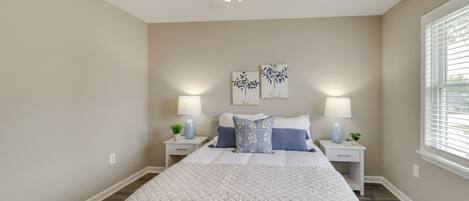A bedroom with a large bed, two bedside tables with lamps, a ceiling fan, and artwork on the wall.