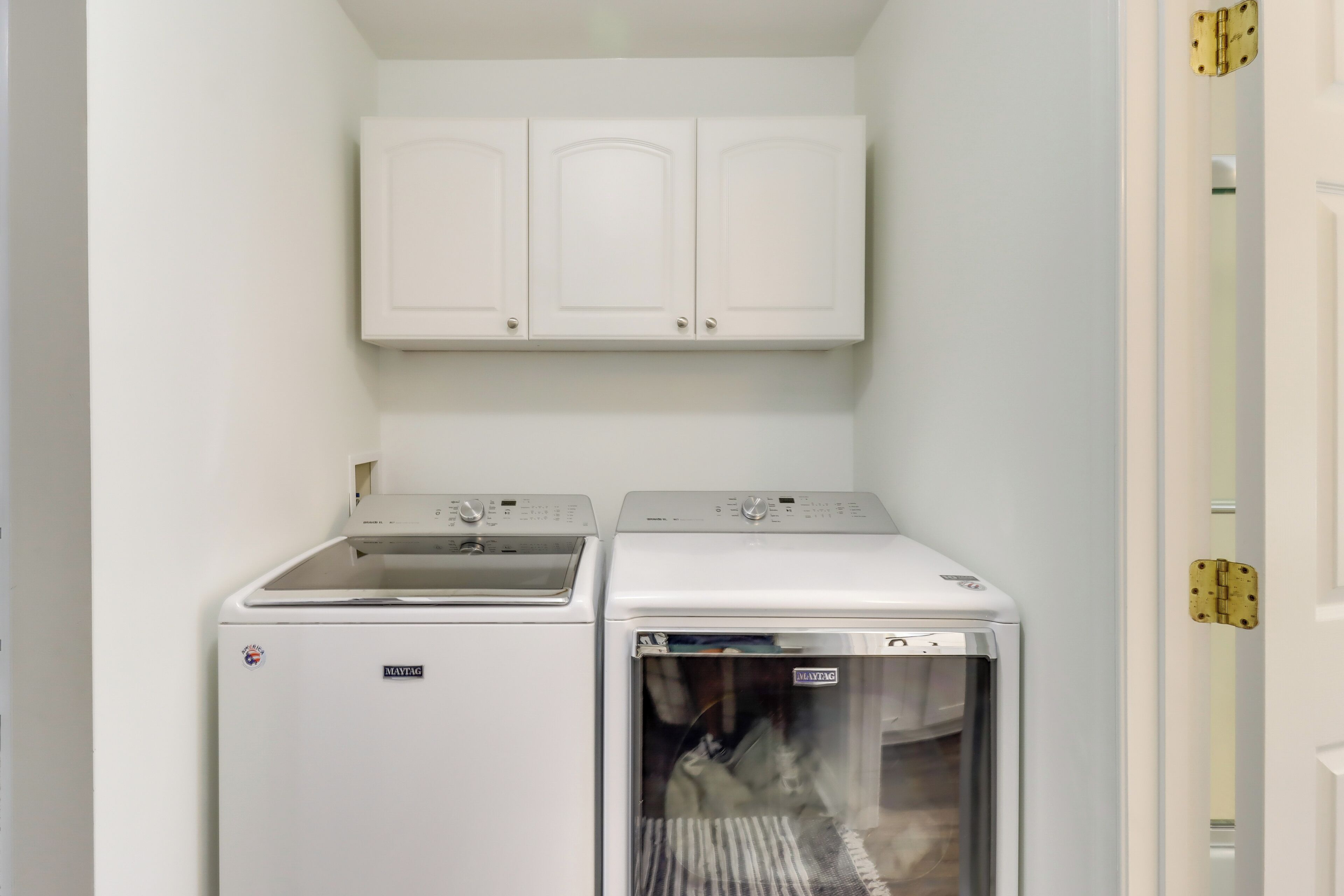 A compact laundry room with two white washing machines and a cabinet above.