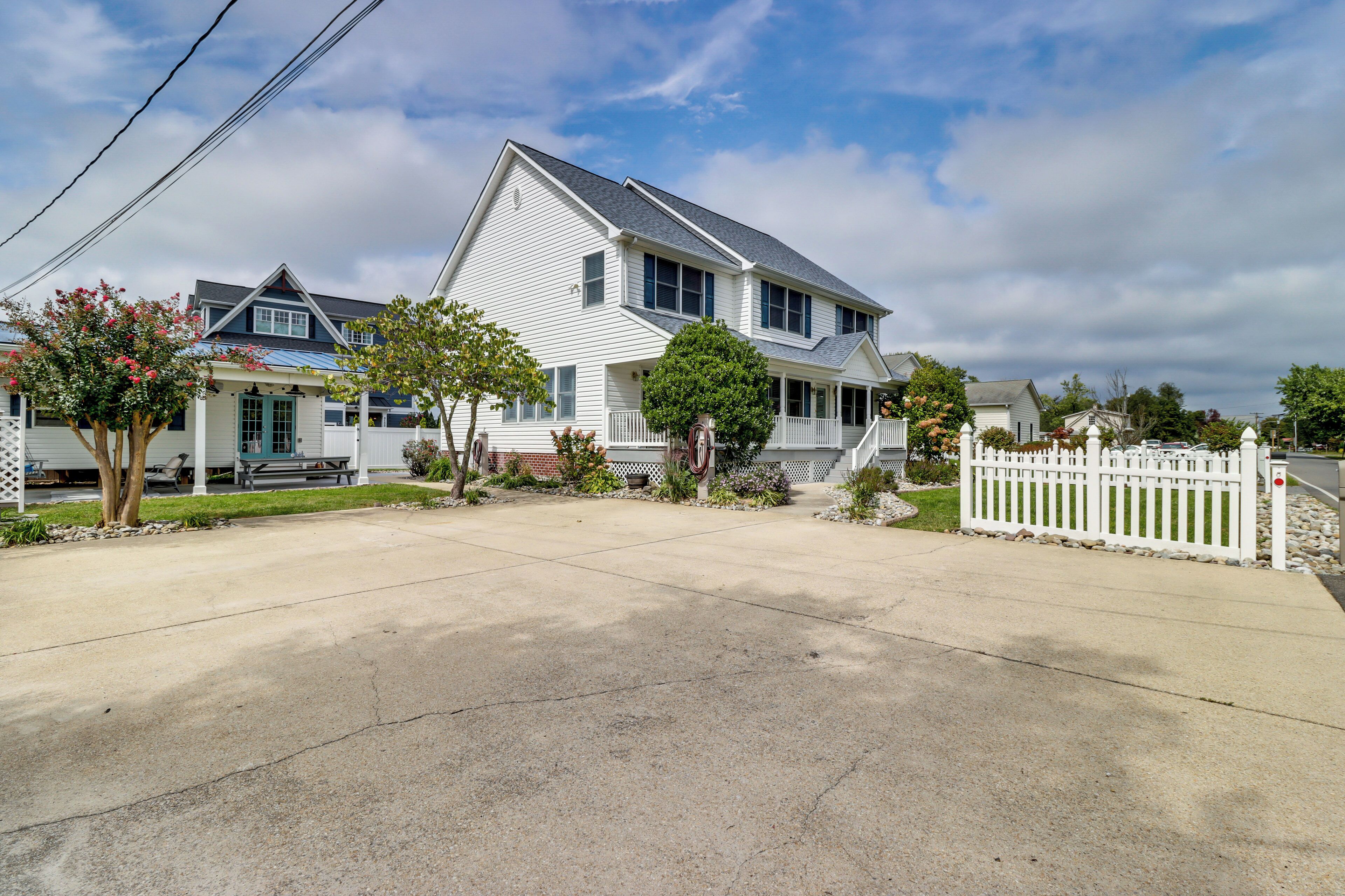 A two-story house with a front porch, a driveway, and a white picket fence.