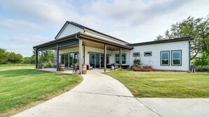 A modern two-story house with a covered patio, a concrete driveway, and a well-maintained lawn. - Lakefront Texas Home on Legacy Ranch (D'Hanis)