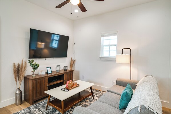 Una sala de estar con un televisor de pantalla plana, un mueble de entretenimiento de madera y un sofá gris con una manta blanca.